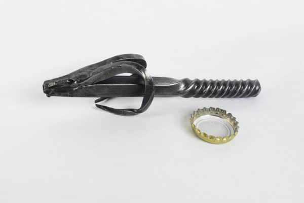 Kovaný otvárak - cap s prispôsobenou rukoväťou vedľa použitého korunkového uzáveru