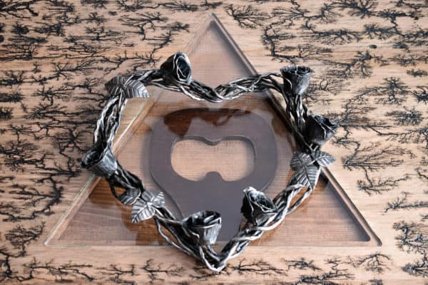 Kovaný veniec v tvare srdca s kovanými ružami a lístkami položený na skle vypáleného stola s AVAJAK logom